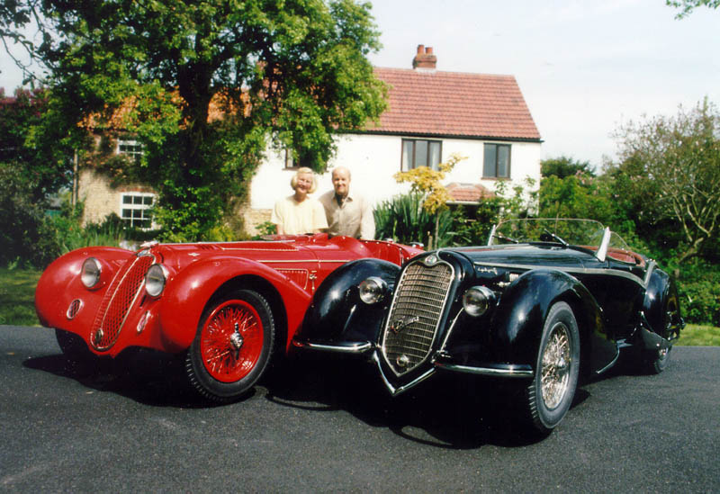 1/15 Scale Alfa Romeos Phyllis and Gerald pose behind two 1/15 scale Alfa Romeos in the driveway.
