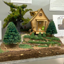 This dollhouse is nestled in the woods with a small still sitting outside near a stream.